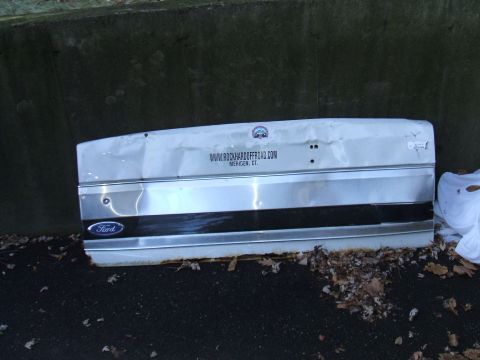 1995 Ford Bronco - A damaged white Ford tailgate with a website address printed on it lies on the ground.