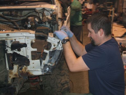 1995 Ford Bronco - A man in blue gloves works on the front end of a white 1992 Ford Bronco in a garage.
