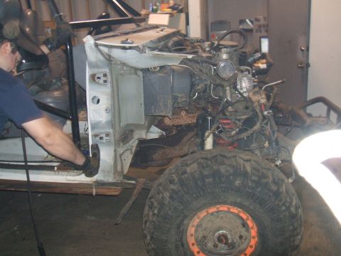 1995 Ford Bronco - A mechanic works on a disassembled white Ford Bronco, revealing its engine and chassis during a rebuild.