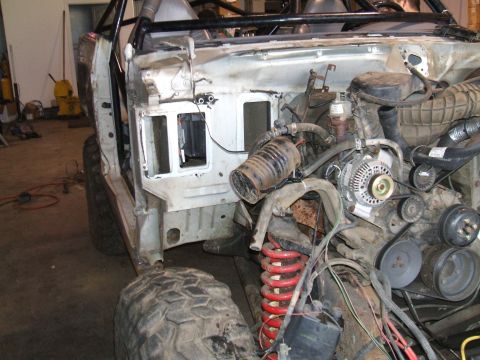 1995 Ford Bronco - The engine bay of a vehicle undergoing extensive modification, showing exposed mechanical parts and a roll cage structure.