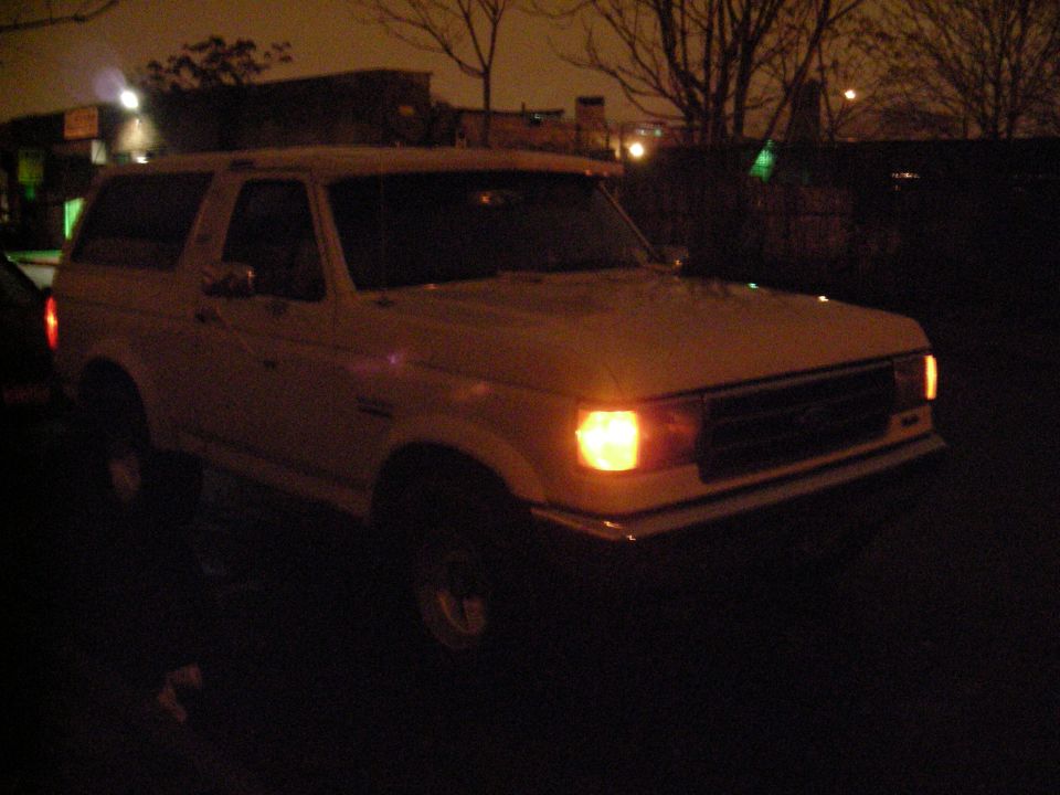1989 Ford Bronco parked at night, front passenger side visible with headlight on