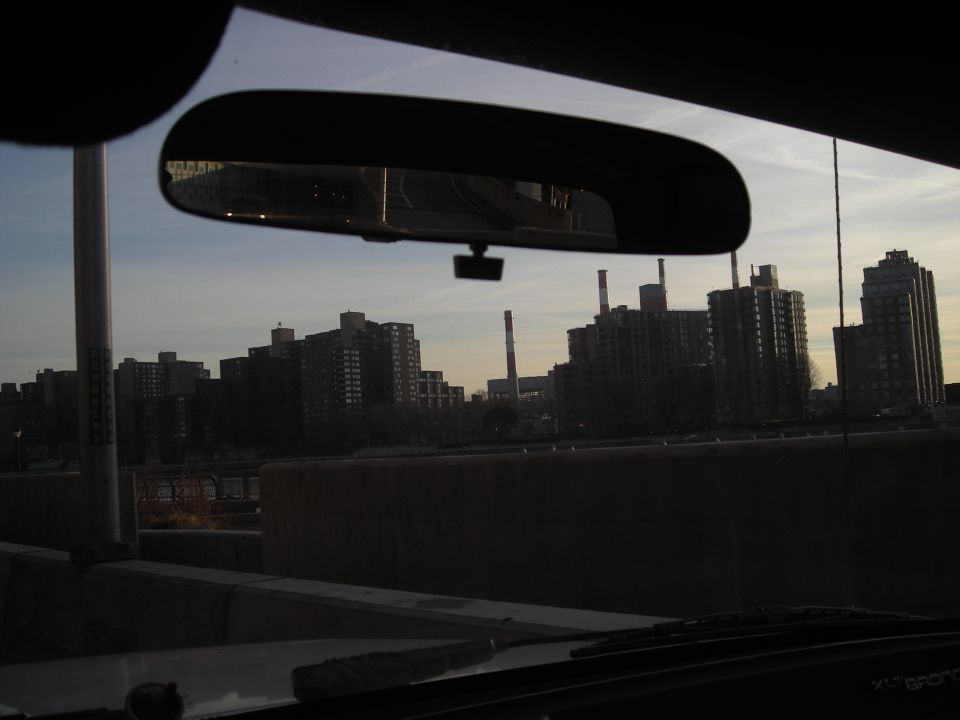 View of city buildings and smokestacks through a car's windshield and rearview mirror