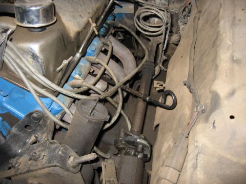 1978 Ford Bronco - Grimy engine bay detail showing a blue Ford V8 block and head with a chrome valve cover and oil filler cap, gray spark plug wires in wire l…
