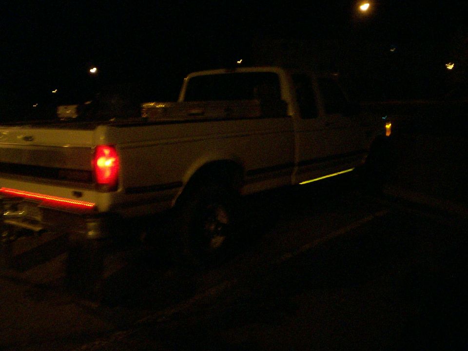 White Ford extended-cab pickup at night with red tailgate light bar