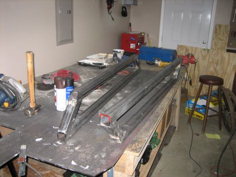 1996 Ford Bronco - A pair of shop-fabricated square-tube rock sliders / nerf bars with angled kick-out legs laid out on a steel-topped workbench in a home gar…
