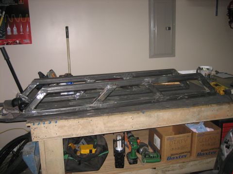 1996 Ford Bronco - A welded ladder-style frame of square steel tubing, a shop-built bumper or skid/rack structure, laid flat on a garage workbench, showing br…