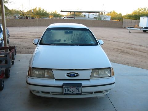 1993 Ford Taurus - A white 1993 Ford Taurus is parked in a driveway with a trailer and other vehicles in the background.