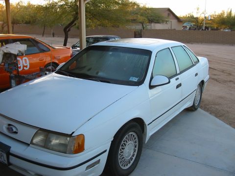 1993 Ford Taurus - A white sedan is parked next to an orange car with the number 99 on its side.