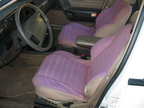 1993 Ford Taurus - The interior of the vehicle features purple seat covers over tan upholstery, with a view of the steering wheel and dashboard.