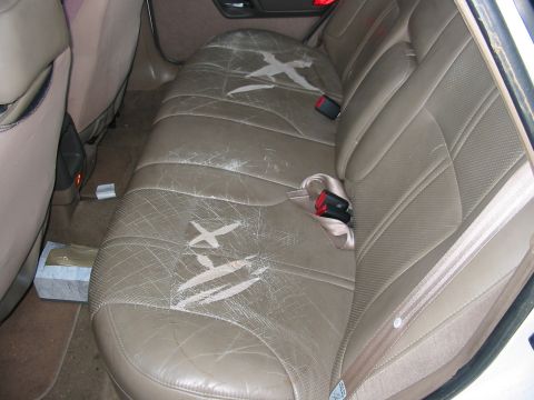 1993 Ford Taurus - Interior view of worn tan leather rear car seats with visible damage and seatbelts.