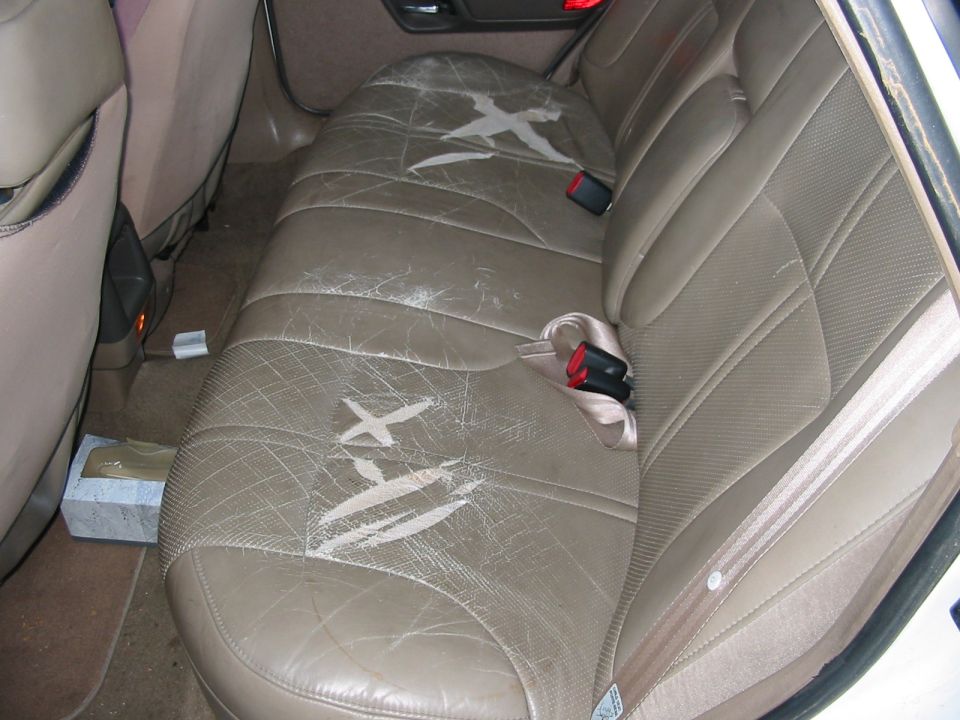 Cracked and torn tan leather rear bench seat in a sedan with worn foam showing
