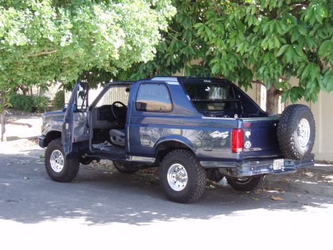 1995 Ford F-150 - This blue SUV, likely a Ford Bronco, is shown with its doors open and a spare tire mounted on the rear.