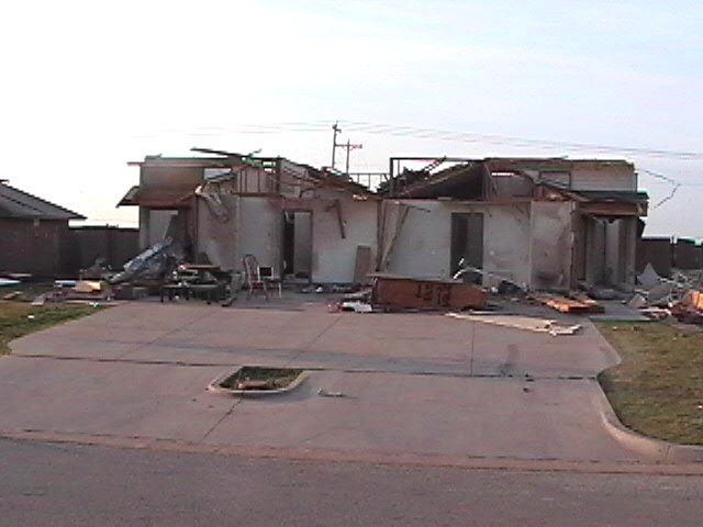 Damaged house with debris scattered on a concrete driveway