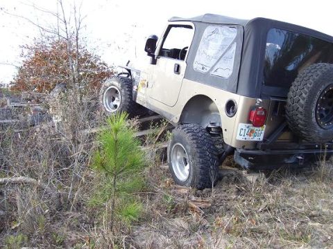 2004 Jeep TJ - A tan Jeep TJ navigates an off-road obstacle course with its spare tire mounted on the rear.