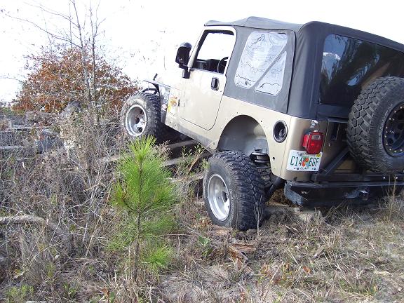 Tan Jeep TJ with soft top on rough terrain, rear view showing spare tire and license plate C14 GGF