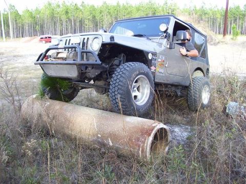 2004 Jeep TJ - A Jeep TJ navigates an obstacle on an off-road trail, with a red vehicle in the background.