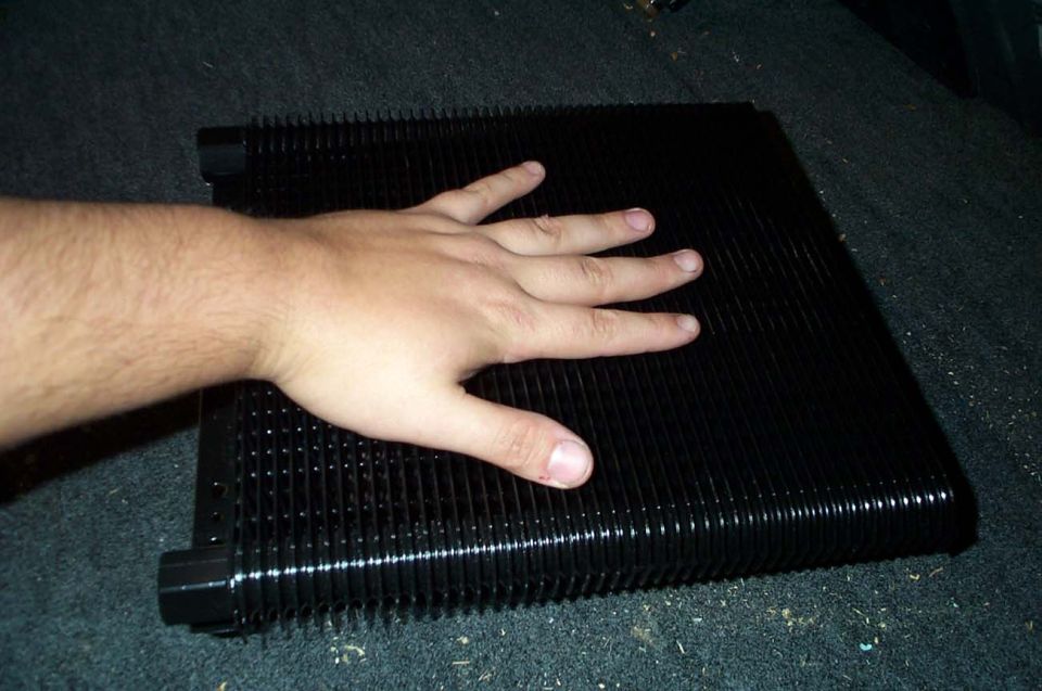 Hand on finned heatsink of large black car audio amplifier for scale on carpet