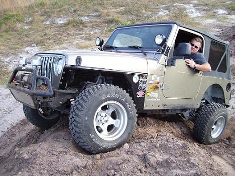 2004 Jeep TJ - A man drives a gold 2004 Jeep Wrangler off-road, navigating a dirt incline.