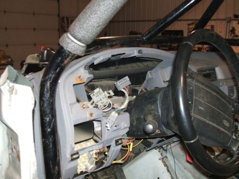 1995 Ford Bronco - The dashboard of a vehicle is disassembled, revealing electrical wiring and a roll cage structure.
