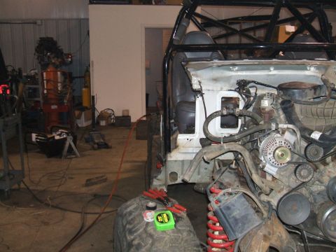 1995 Ford Bronco - The front end of a vehicle is disassembled in a workshop, revealing the engine and suspension components.