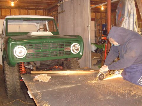 1974 Ford Bronco - A man grinds metal in front of a green Ford Bronco, which appears to be undergoing restoration in a garage.