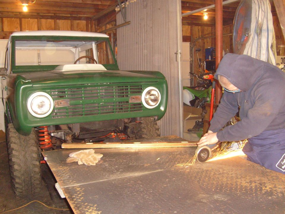 Green 1970s Ford Bronco with white top, front view, being worked on in a garage