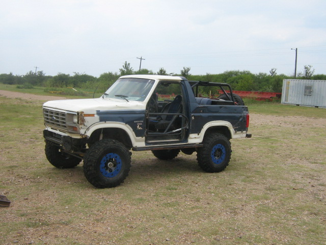 Two-tone blue and white topless Ford Bronco on blue wheels, dirt lot