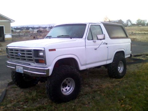 1983 Ford Bronco - This lifted 1980 Ford Bronco features a prominent grille and large off-road tires, captured in a three-quarter front view.