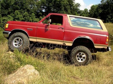 1988 Ford Bronco - This 1988 Ford Bronco is shown off-road, navigating through tall grass and rocks.