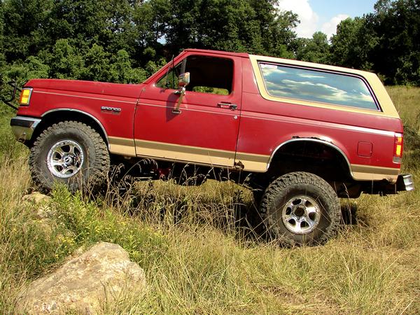 1988 Ford Bronco driving on grassy terrain with trees in background