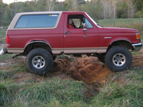 1988 Ford Bronco - A red 1988 Ford Bronco navigates a challenging off-road path with a driver inside.