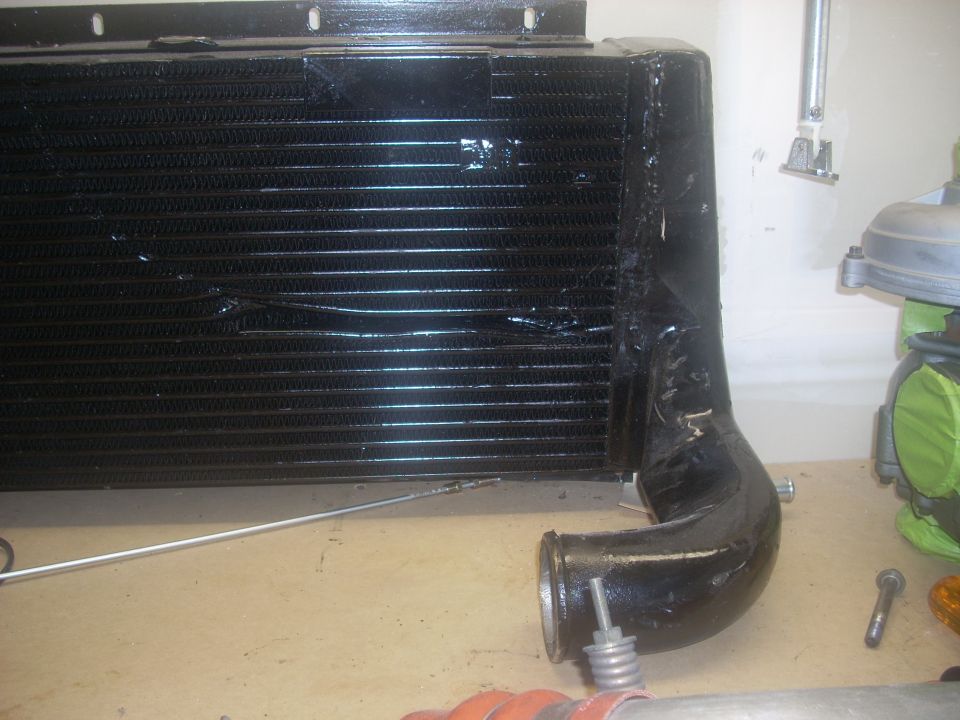 Black intercooler with black piping attached. Supermotors.net logo visible