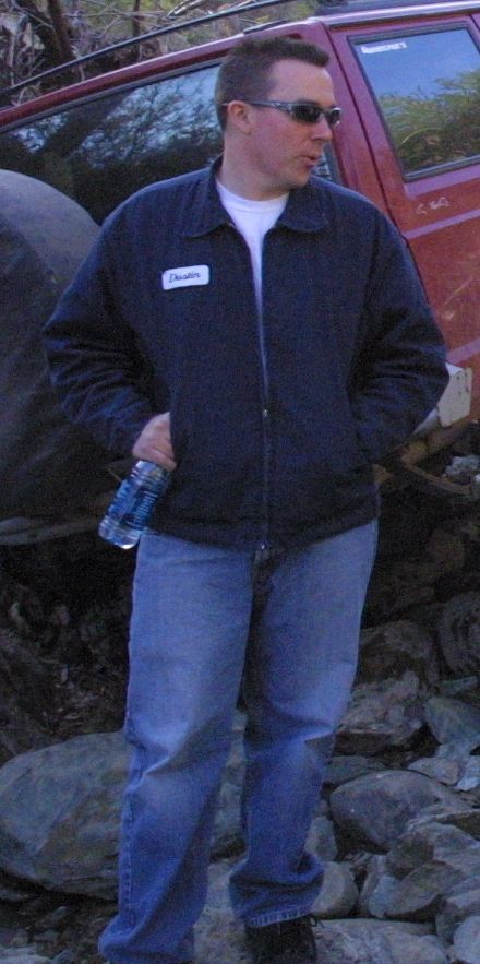 1994 Ford Bronco - Man stands next to a red Jeep Cherokee, possibly during an off-road event.