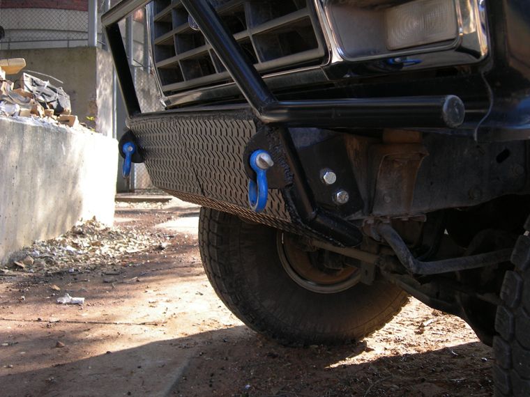 Front bumper with diamond plate texture and blue tow hooks on a truck, grille visible above