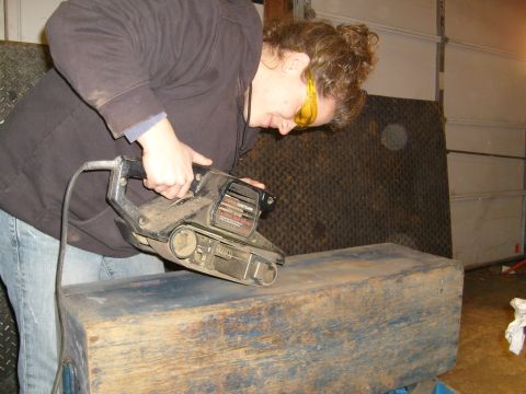 1974 Ford Bronco - A person sands a weathered wooden box with a belt sander in a garage setting.