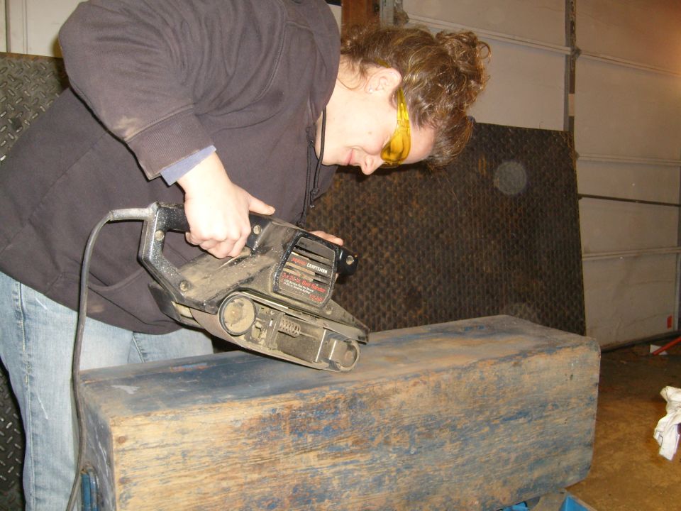 Person sanding a wooden box with a belt sander