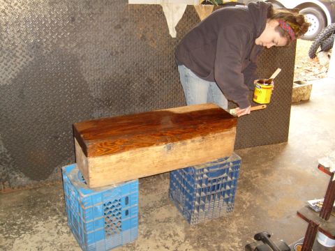 1974 Ford Bronco - A person applies stain to a wooden chest supported by blue milk crates in a garage.