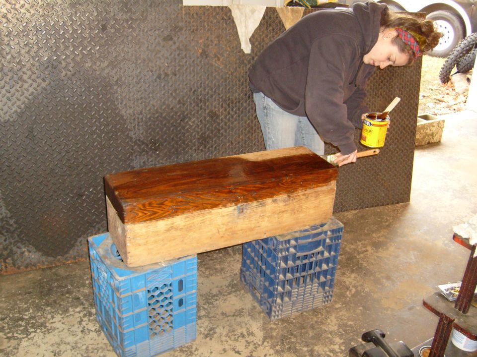 Person staining a wooden chest on top of milk crates
