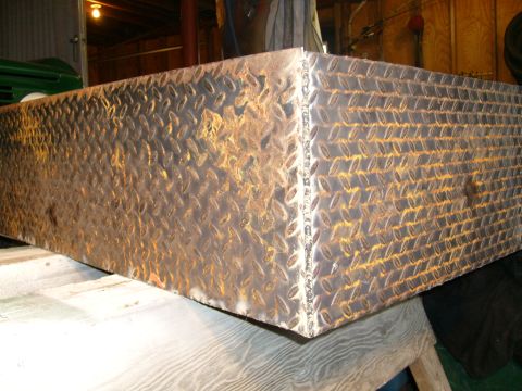 1974 Ford Bronco - A metal toolbox with a diamond plate texture sits on a wooden surface indoors.