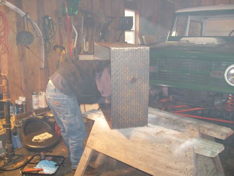 1974 Ford Bronco - A person works in a garage next to the front of a green 1974 Ford Bronco.