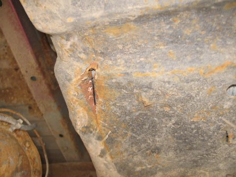 1995 Ford Bronco - Underbody close-up of a heavily surface-rusted sheetmetal panel with a torn split where the metal has cracked open and peeled back, exposin…