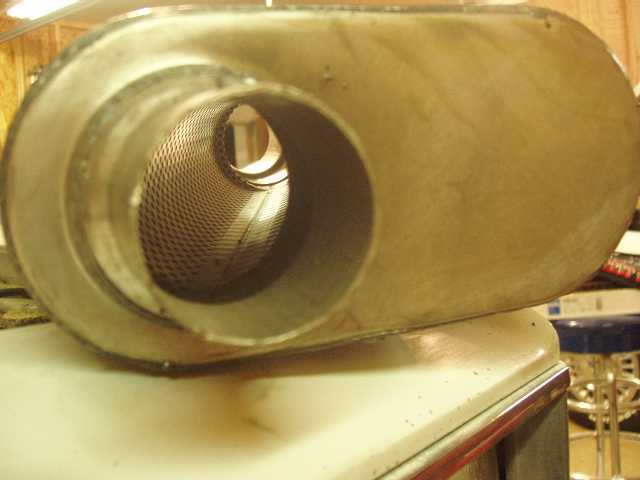 Oval performance muffler on a countertop, showing perforated core tube through open inlet