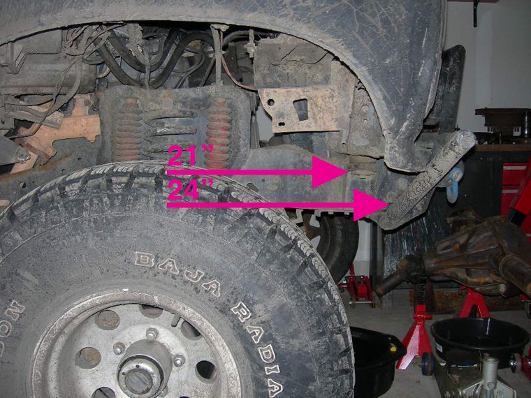 Close-up of vehicle suspension with measurements marked by pink arrows. Tire tread reads 'BAJA RADIAL'
