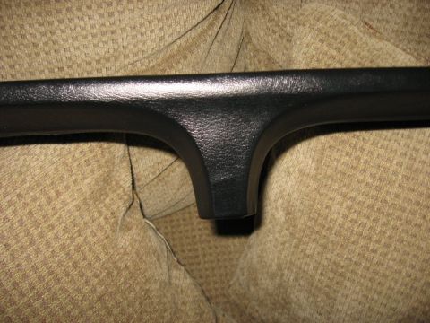 1978 Ford Bronco - Close-up of a black interior dashboard trim piece, likely from a vintage vehicle, set against a textured tan fabric background.