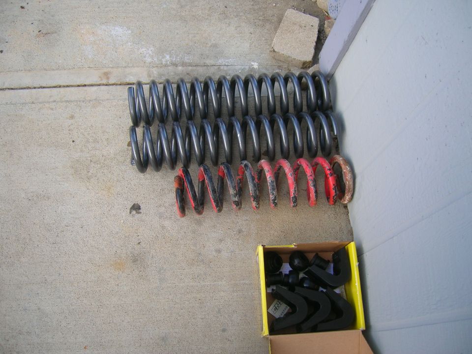 Two sets of coil springs, one gray and one red, next to a box of black suspension hardware