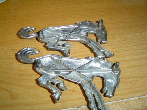 1979 Ford Bronco - Two chrome horse emblems are shown on a wooden surface, one with visible part numbers.