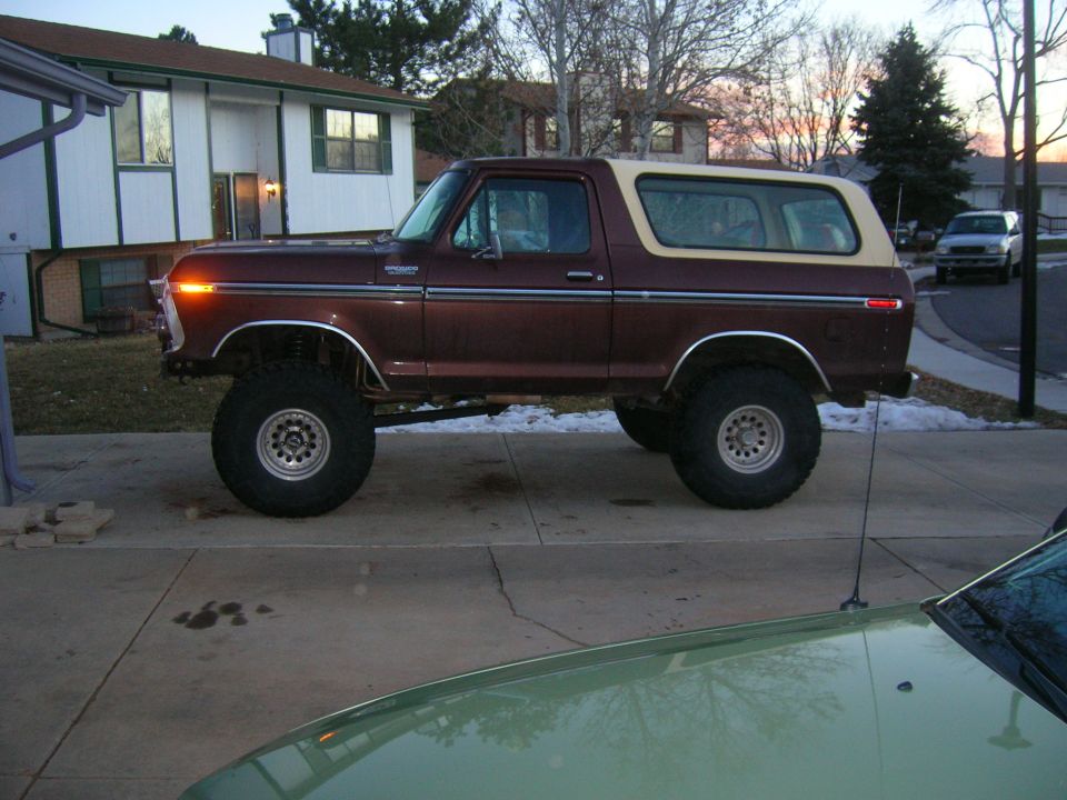 Maroon 1978 Ford Bronco with tan top, lifted suspension, and large tires parked on a driveway