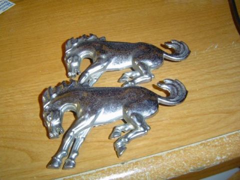 1979 Ford Bronco - Two chrome horse emblems, possibly for a car, are shown on a wooden surface.