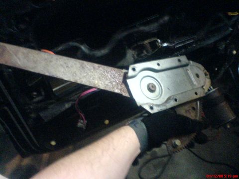 1986 Ford Bronco - Close-up view of a vehicle's window regulator mechanism, showing a rusty metal arm and a silver plate.