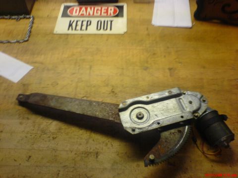 1986 Ford Bronco - Power window regulator mechanism with motor and gear. 'DANGER KEEP OUT' sign is visible in the background.